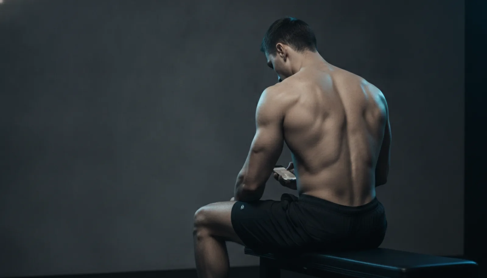A man seen from behind sitting on a gym bench looking at his phone