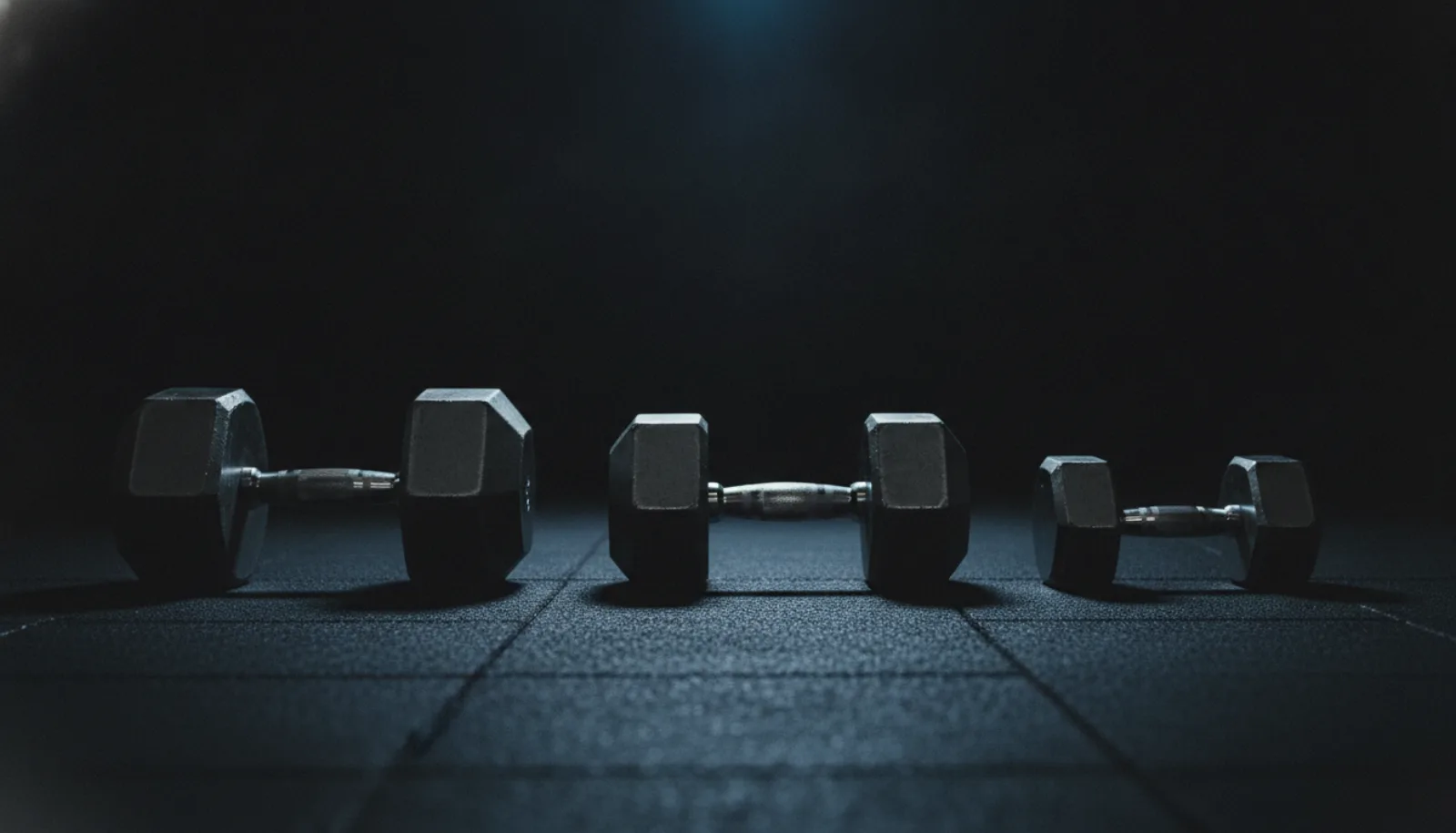 Three dumbbells of different sizes lined up on a gym floor